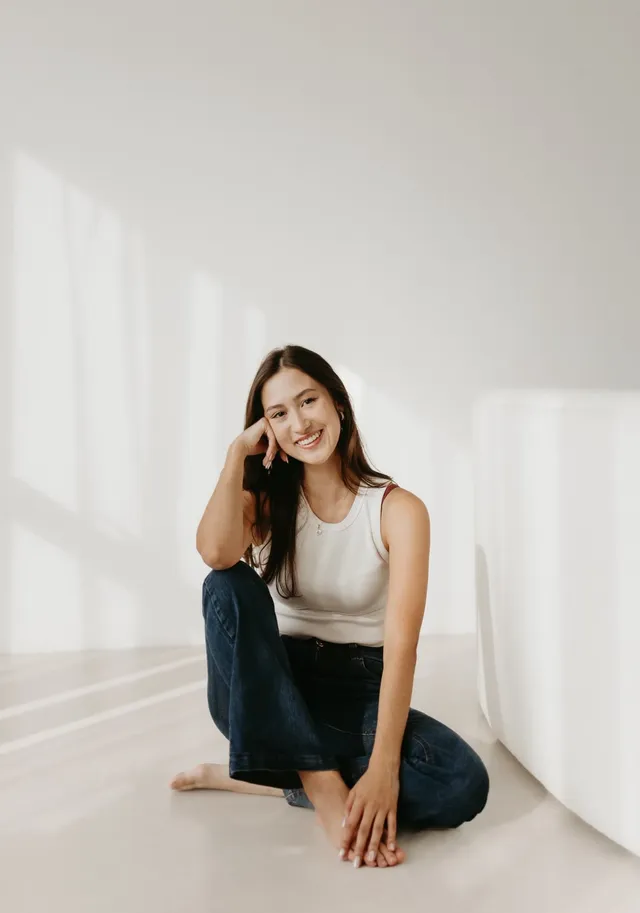 luisa oliveira, sentada no chão de um estúdio claro, sorrindo